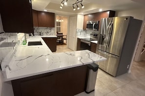 A modern kitchen with a marble countertop, stainless steel appliances, and a dining area with a chandelier. - 3-bedroom house in terrific Sarasota with Heated pool ,close to Airport beaches (Sarasota)