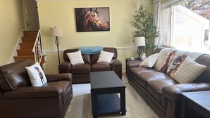 Ein Wohnzimmer mit einem braunen Ledersofa, einem schwarzen Couchtisch, einer Treppe, einem Gemälde und einer Topfpflanze.