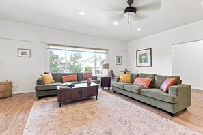 A spacious living room with a large window, a ceiling fan, and a fireplace. - Sun Lake Retreat – Banks Lake Getaway (Coulee City)