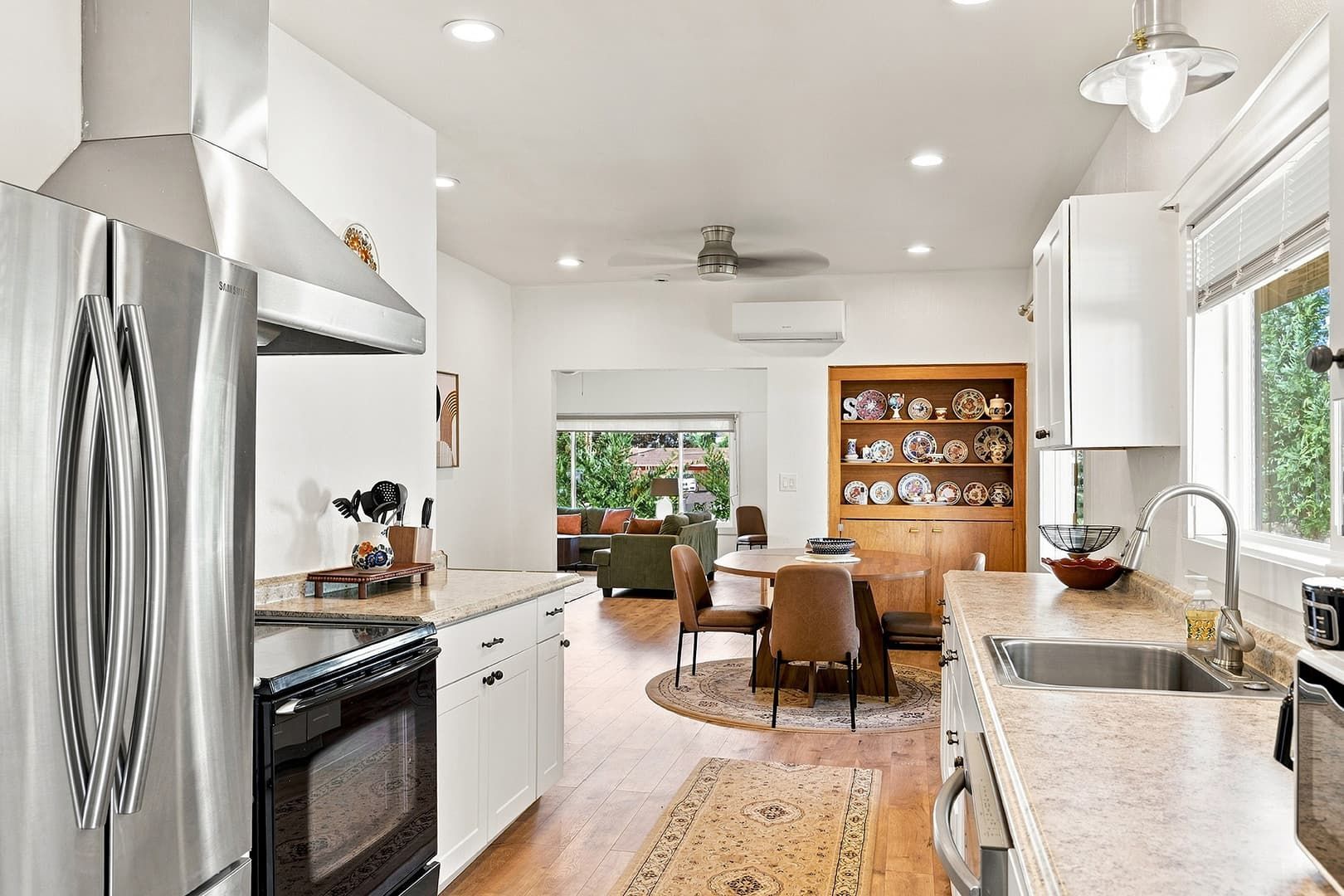 A modern kitchen with stainless steel appliances, a dining area with a round table, and a view of greenery outside.