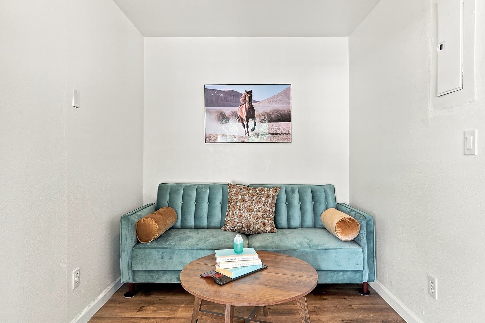 Una habitación con un sofá color turquesa, una mesa de centro redonda de madera y un cuadro enmarcado en la pared.