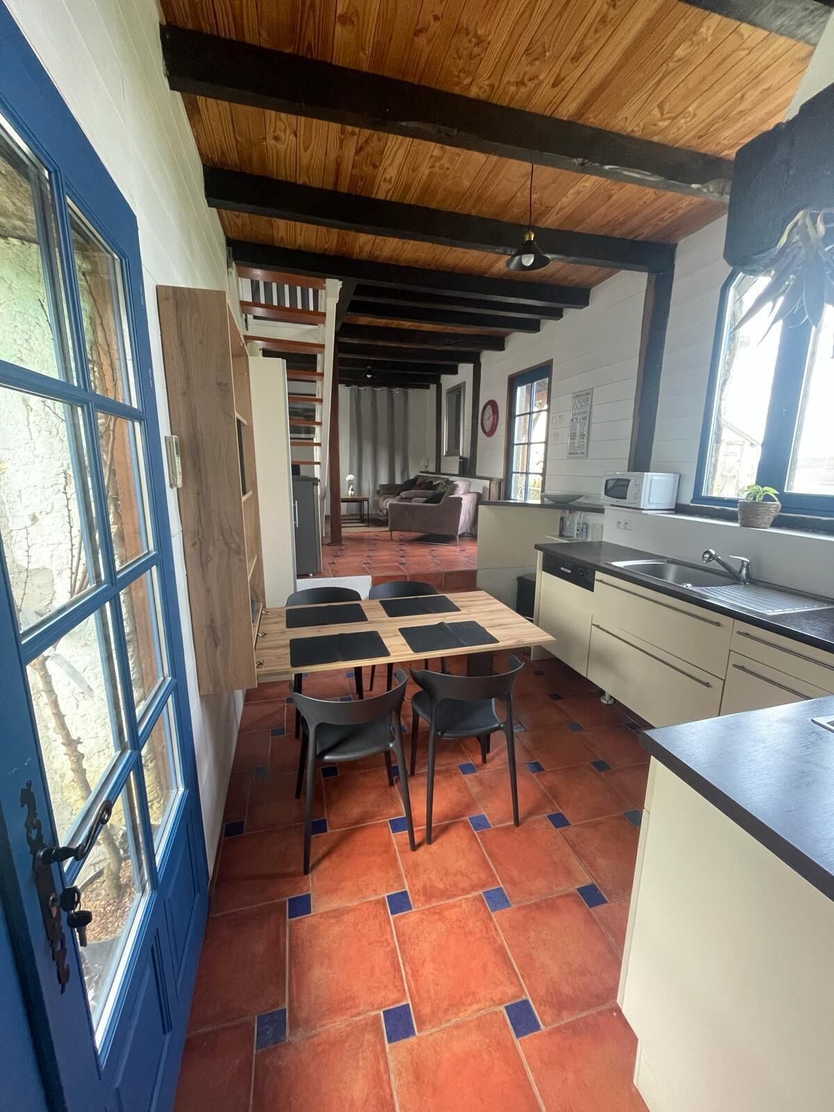 A dining area with a wooden table and chairs, a kitchen with a sink and microwave, and a blue door with windows.