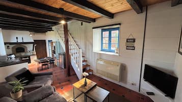 Una sala de estar con sofá, mesa de centro, televisor, chimenea y una escalera que lleva a una cocina.