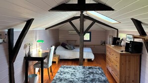 Ein Schlafzimmer im Loftstil mit schrägem Dach, einem Bett, einem Schreibtisch mit Lampe, einer Kommode und einem Fenster.