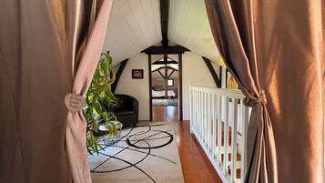 A cozy room with a wooden floor, a black chair, a bed, and a white railing.