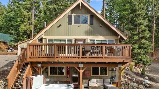 A two-story cabin with a balcony, outdoor seating, and a hot tub.