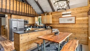 A wooden cabin interior with a kitchen, dining area, and a large window.