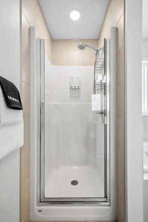Eine begehbare Glasdusche mit weißem Boden, einer Handbrause und einem Handtuchhalter mit einem Handtuch.
