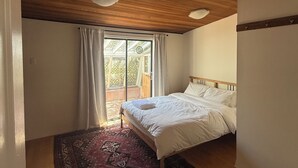 A bedroom with a wooden ceiling, a bed with white linens, a patterned rug, and a large window with curtains. - 2 Bedroom Semi-Waterfront Cottage in Vesuvius, Salt Spring Island (Salt Spring Island)
