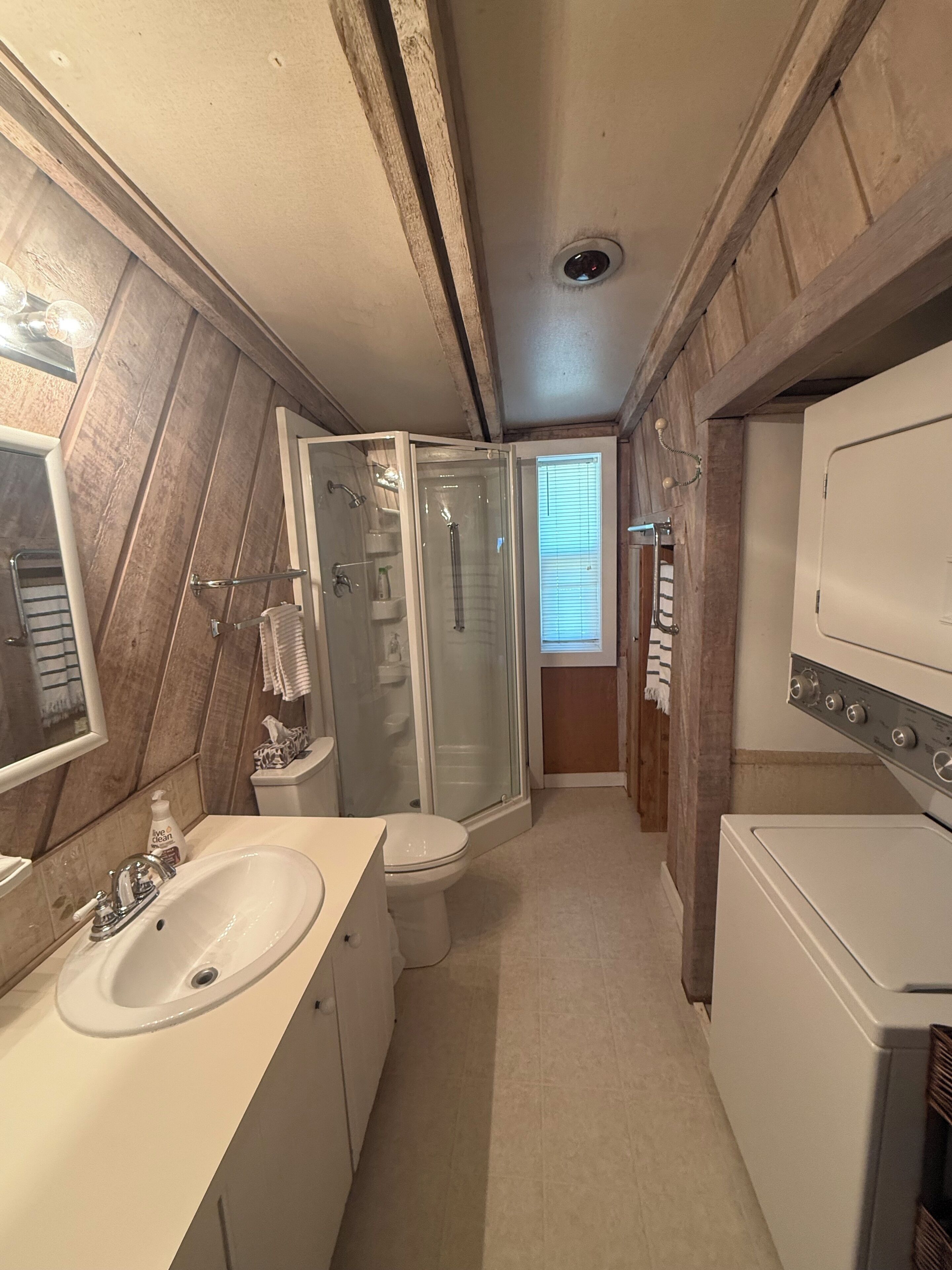 A compact bathroom with a shower, toilet, sink, and a washing machine.