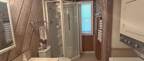 A compact bathroom with a shower, toilet, sink, and a washing machine.