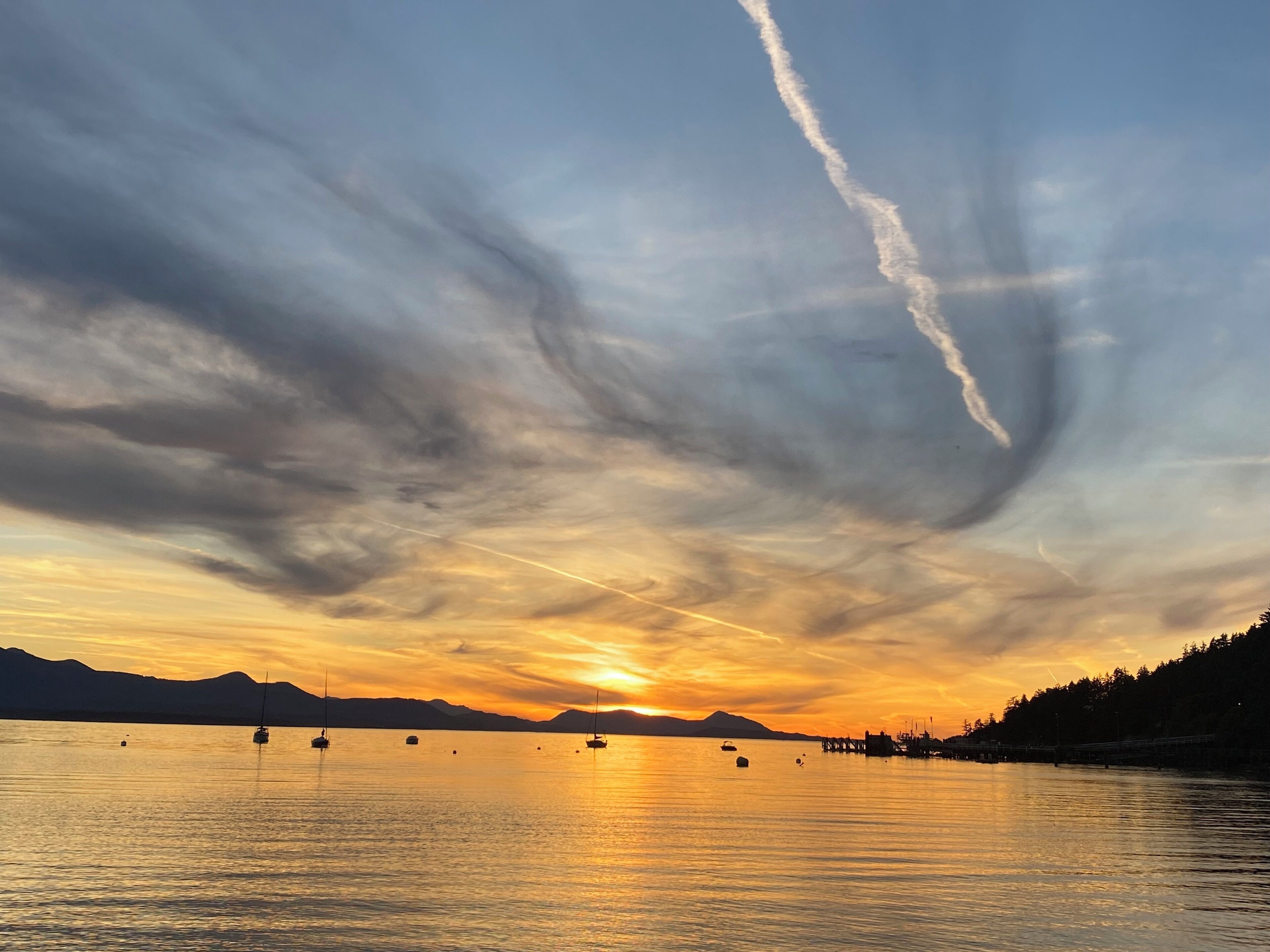 Een zonsondergang boven een rustig wateroppervlak met boten en een pier.