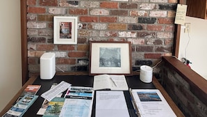 A rustic brick wall with a wooden shelf holding pottery, a framed picture, and a map. - 2 Bedroom Semi-Waterfront Cottage in Vesuvius, Salt Spring Island (Salt Spring Island)