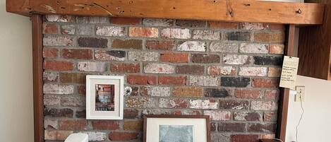 A rustic brick wall with a wooden shelf holding pottery, a framed picture, and a map.