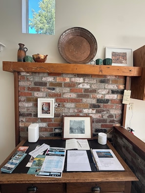 A rustic brick wall with a wooden shelf holding pottery, a framed picture, and a map.