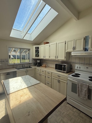 A kitchen with skylights, a sink, cabinets, a microwave, and a stove.