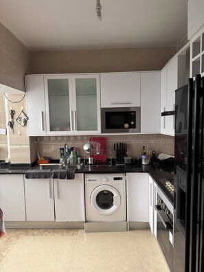 A kitchen with white cabinets, a microwave, a washing machine, and a refrigerator.