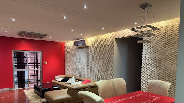 A modern living room with a red wall, a sofa, a table with a red tablecloth, and a patterned wall. - Apartment M15 (Luanda)