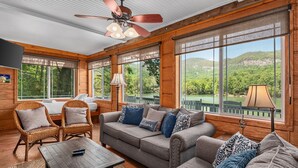 A cozy room with a ceiling fan, large windows, a sofa, a table, and wicker chairs.