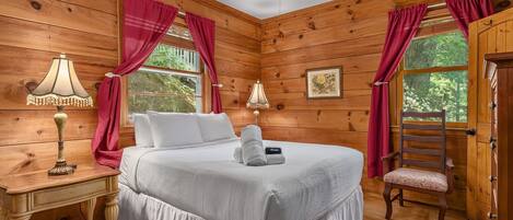 Un dormitorio de cabaña de madera con cama, mesita de noche, lámpara, silla y ventilador de techo.