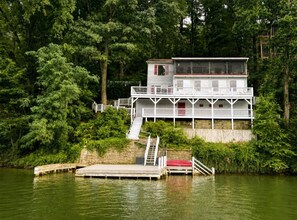A multi-story house with a dock and a staircase leading to a red boat.