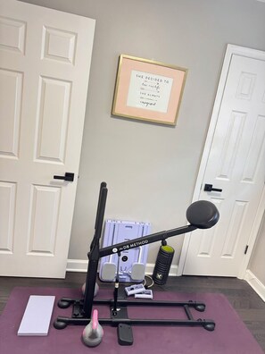 Ein Heimfitnessstudio mit Ergometer, Gewichten und einem motivierenden Spruch an der Wand.