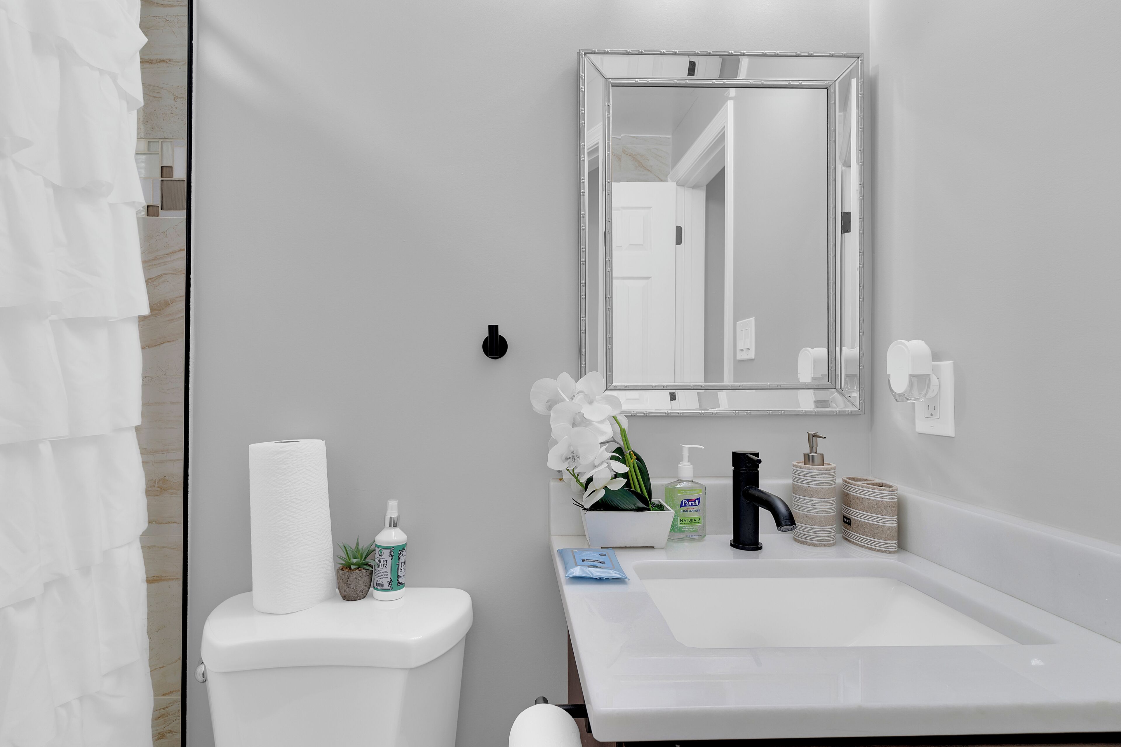 Ein Badezimmer mit einem weißen Waschbecken, einem Spiegel, einer Toilette und einer Duschvorhang.