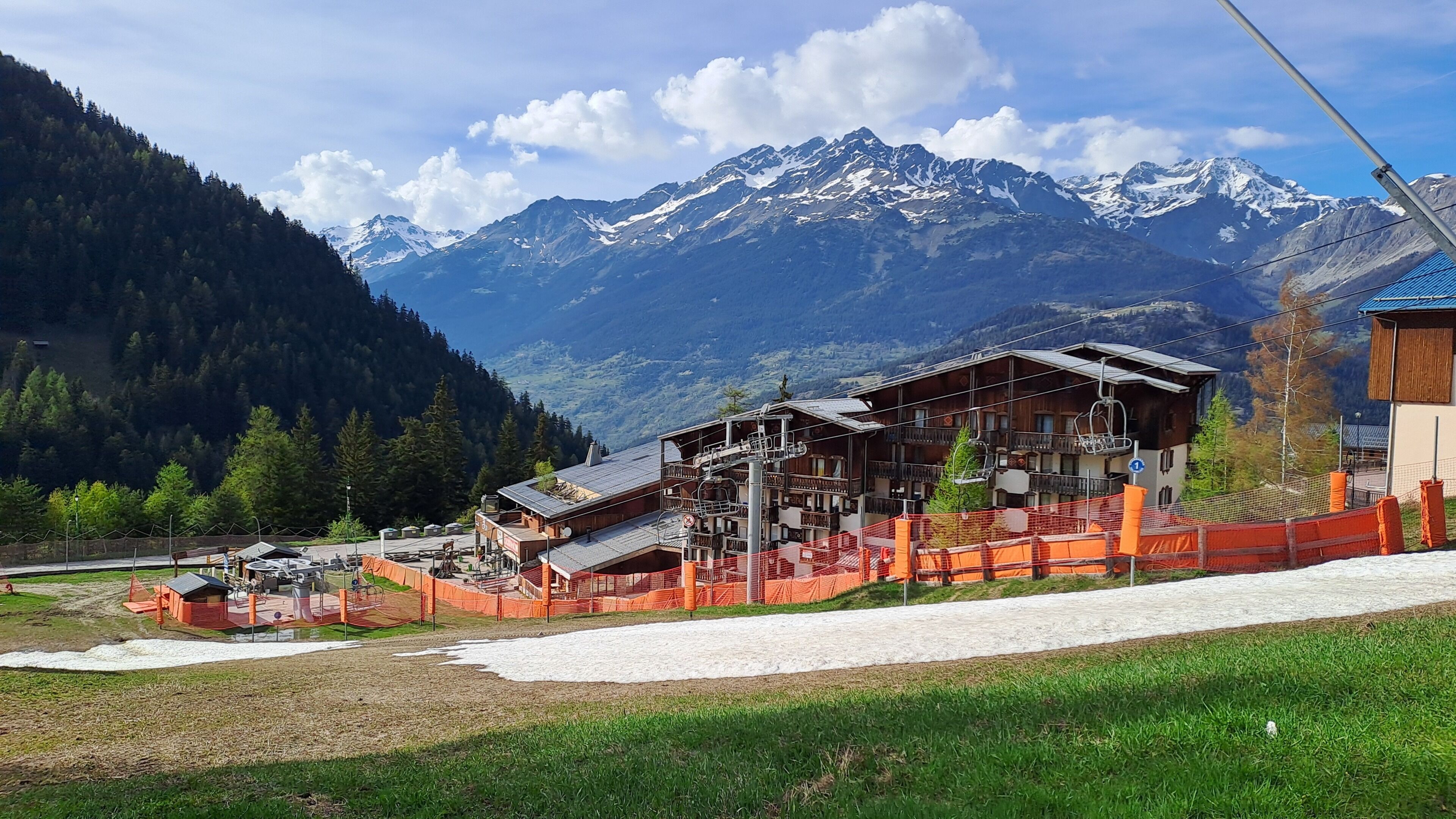 A mountain lodge with a ski lift, surrounded by snow-covered peaks and a forested valley.