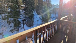 Une terrasse en bois dotée d’une balustrade, qui offre une vue sur un paysage enneigé, avec des arbres et un ciel dégagé.
