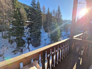 A wooden deck with a railing overlooking a snowy landscape with trees and a clear sky.