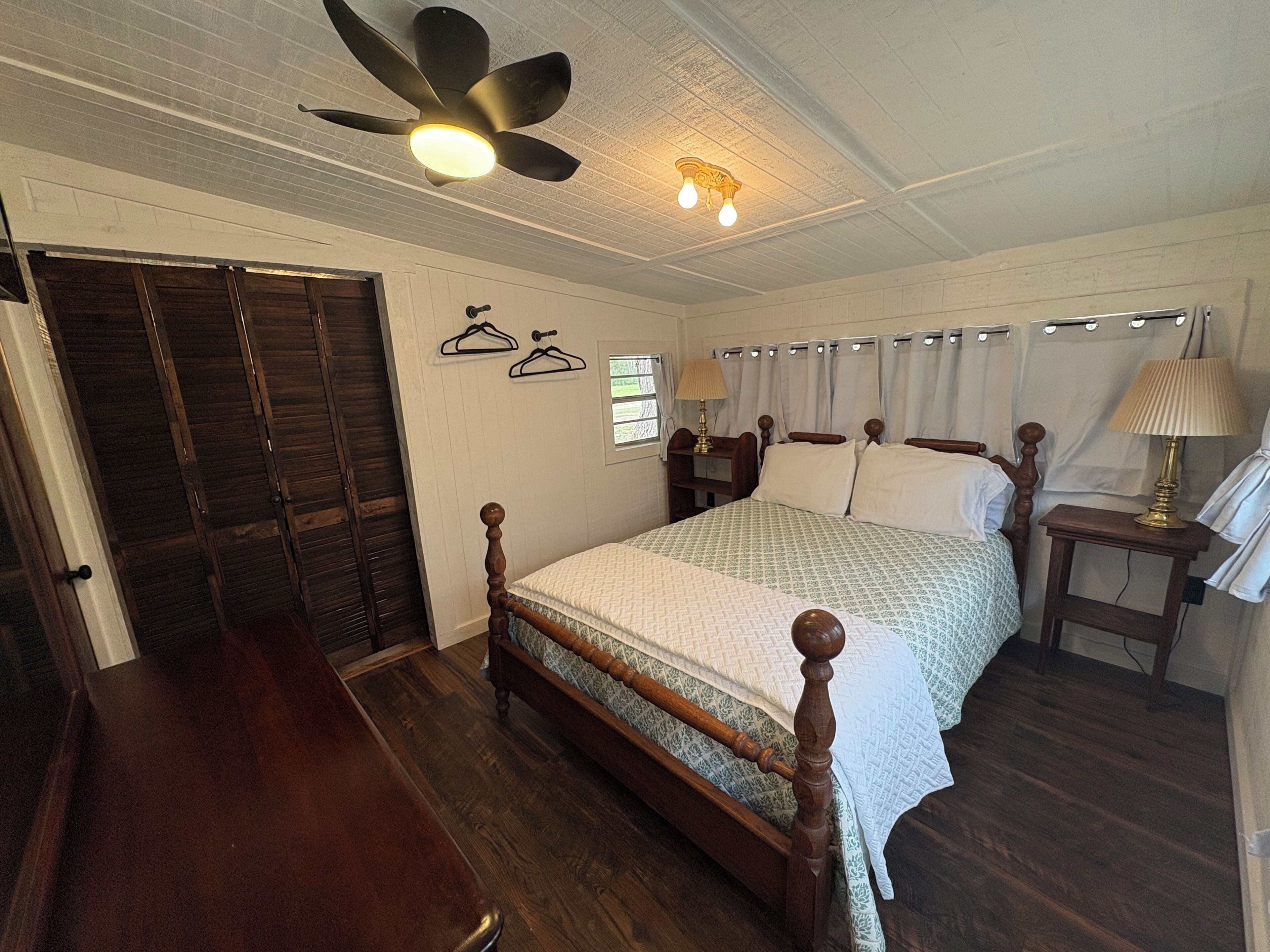 A bedroom with a wooden bed, a ceiling fan, a nightstand, and a wardrobe.