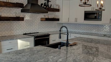 A modern kitchen with a large granite island, pendant lights, and white cabinetry.