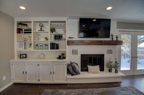 A living room with a fireplace, a mounted TV, and a built-in bookshelf. - Backyard Oasis with In-ground Pool, Fire Pit, and Gazebo! (Onalaska)
