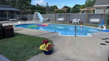 Un jardin avec une piscine, un toboggan et une terrasse en bois.
