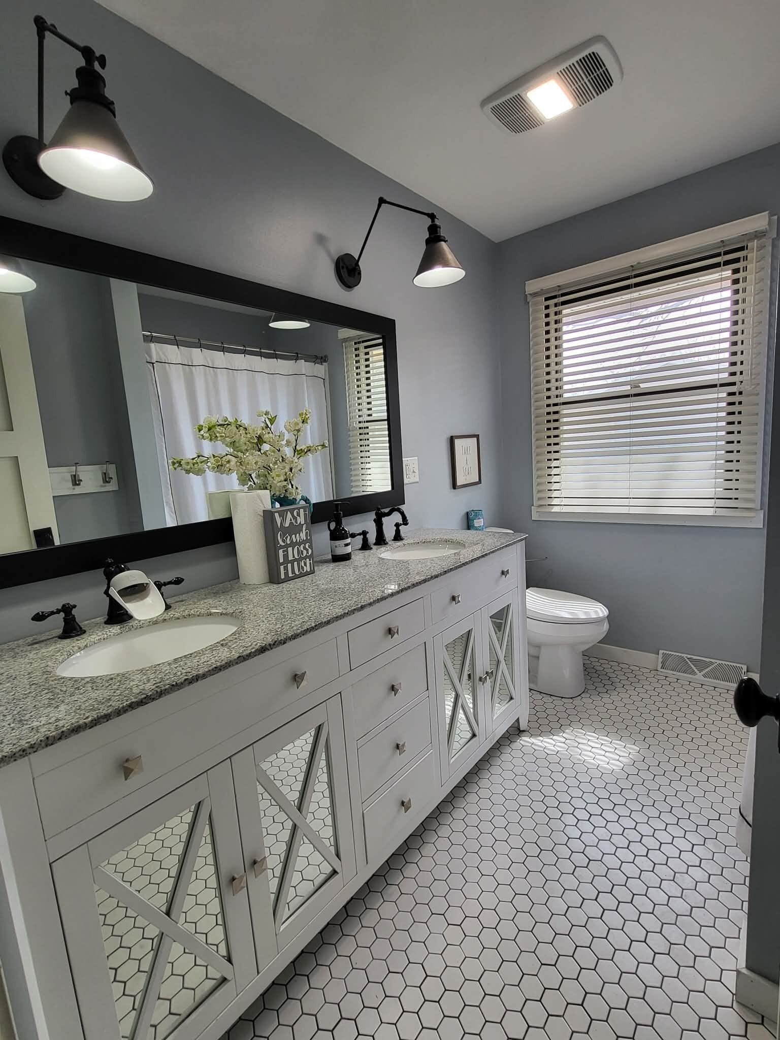 A bathroom with a white vanity, a large mirror, a sink, and a toilet.