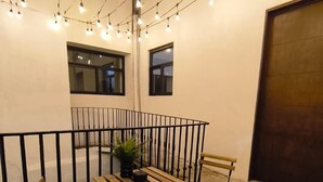 Un patio con una mesa y sillas de madera, luces colgantes y un felpudo.