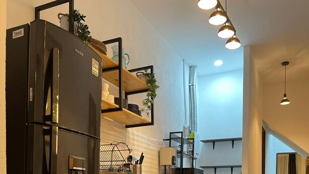 Una cocina moderna con un refrigerador negro, repisas de madera, cestas de mimbre y una lavadora.