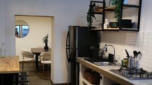 Una cocina moderna con refrigerador empotrado, un área de comedor con espejo redondo y una lámpara colgante.