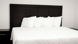 Ein ordentlich bezogenes Bett mit weißen Leinen und Kissen, ein dunkles Kopfteil und ein Nachttisch daneben.