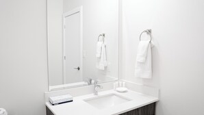 Ein modernes Badezimmer mit einem weißen Waschbecken, einem großen Spiegel und einem Handtuchhalter.