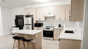 Eine moderne Küche mit Holzausbau, einer eingebauten Mikrowelle, einem Kühlschrank, einem Backofen und einem Spülbecken. Zwei Barhocker und eine kleine Kochinsel mit Arbeitsplatte sind ebenfalls vorhanden.