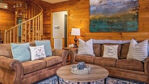 A cozy room with a wooden staircase, a sofa set, a coffee table, and a painting on the wall. - New Listing! Cabin On The Lake, Hot Tub, Game Rm! (Sevierville)