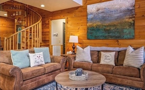 A cozy room with a wooden staircase, a sofa set, a coffee table, and a painting on the wall. - New Listing! Cabin On The Lake, Hot Tub, Game Rm! (Sevierville)