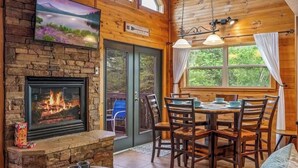 A cozy cabin interior with a fireplace, dining table, chairs, and a television mounted on the wall. - New Listing! Cabin On The Lake, Hot Tub, Game Rm! (Sevierville)