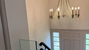 A staircase with a glass railing, a chandelier, and a white door with windows. - Equestrian Derby Escape (Louisville)