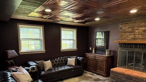 A room with a dark brown leather sofa, a fireplace, and two windows with white frames. - Equestrian Derby Escape (Louisville)