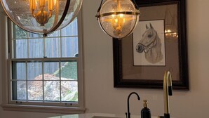 A kitchen with a large window, a hanging spherical chandelier, a framed horse painting, and a modern faucet. - Equestrian Derby Escape (Louisville)