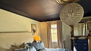 A bedroom with a bed, a chandelier, a dresser, and a window with curtains. - Equestrian Derby Escape (Louisville)
