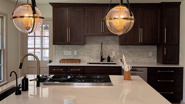 A modern kitchen with dark wooden cabinets, a white marble countertop, and two pendant lights. - Equestrian Derby Escape (Louisville)