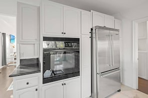 Una cocina con armarios blancos, un refrigerador de acero inoxidable y un horno empotrado.